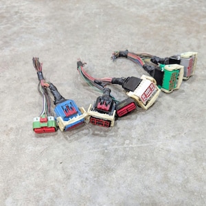 May include: A collection of five automotive electrical wiring harness connectors featuring multi-colored plastic housings in blue, green, red, white, and black, each attached to a bundle of thin, multi-colored insulated copper wires.