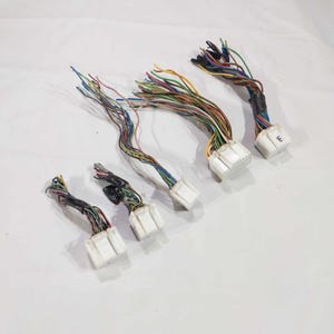 Puede incluir: Varios mazos de cables multicolores con conectores blancos. Los cables son de varios colores, incluyendo azul, verde, rojo y amarillo. Los conectores son rectangulares y tienen múltiples pines.