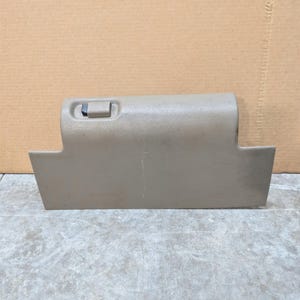 Puede incluir: Una puerta de guantera de automóvil en color beige con una superficie de plástico texturizado, un mecanismo de cierre rectangular con un botón negro y un borde superior ligeramente curvado. El panel tiene una forma rectangular ahusada.