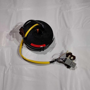 May include: A black steering column with a yellow wire and a grey connector. The column has a red label that says "VERIFY HARNESS".