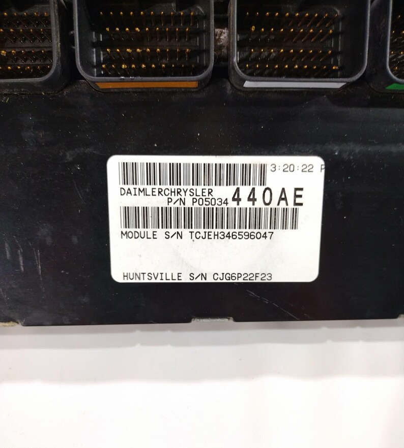 May include: A black electronic control module with multiple connectors. A white label displays "DAIMLERCHRYSLER" and "440AE" along with other text and barcodes. The module is likely for automotive use.