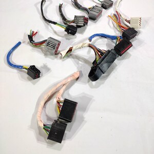 May include: Assortment of automotive electrical connectors with multi-colored wires. The connectors are black, gray, and white, with wires in various colors including red, green, yellow, and blue. The wires are bundled and some are wrapped in protective sheathing.