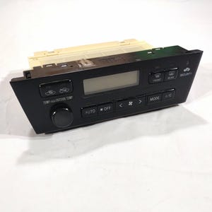 May include: Black car air conditioning control panel with buttons for temperature, fan speed, and A/C. Features a digital display and buttons labeled "AUTO", "OFF", "FRONT", "REAR", and "SECURITY".