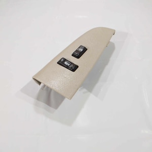 May include: Beige plastic automotive switch panel with two black buttons. The buttons have raised lettering and symbols.