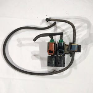 May include: An automotive part featuring a cluster of components with colored connectors and black tubing. The connectors are in shades of brown, black, and blue. The tubing is black and curves around the components.