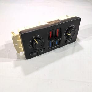 May include: Black car climate control panel with knobs, sliders, and buttons. The panel has a beige frame and features controls for fan speed, temperature, and air direction. The sliders are marked with red and blue indicators. The panel is likely for a vehicle.