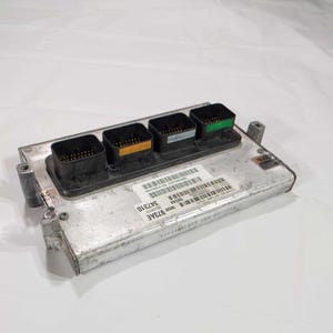 May include: A silver-colored electronic control module with four black connectors. The connectors have colored accents in orange and green. The module has a barcode sticker with the numbers 347310 and 973AE.