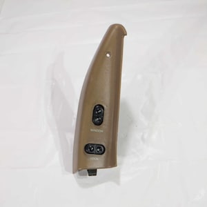 Puede incluir: Un panel de puerta de coche de plástico marrón con dos botones. El botón superior está etiquetado como "Ventana" y el botón inferior está etiquetado como "Bloqueo".