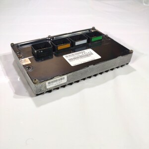 May include: A rectangular, silver electronic control module with four black connectors, each with a different coloured accent. A white label with black text and a barcode is affixed to the top. The module is on a white background.