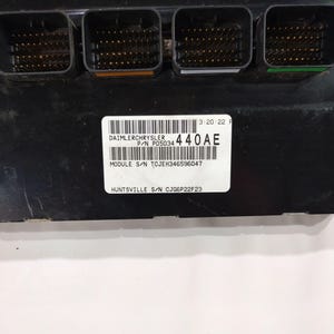 May include: A black electronic module with four connector ports. The module has a white label with the text "DAIMLERCHRYSLER" and "440AE". Additional text includes "MODULE S/N TCJEH346596047" and "HUNTSVILLE S/N CJG6P22F23".