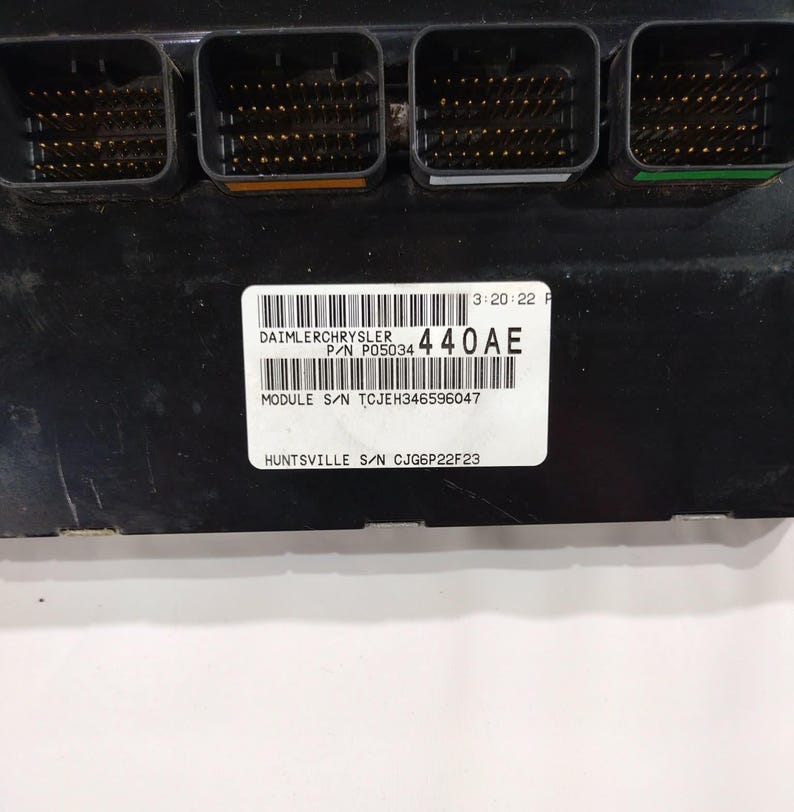 May include: A black electronic module with four connector ports. The module has a white label with the text "DAIMLERCHRYSLER" and "440AE". Additional text includes "MODULE S/N TCJEH346596047" and "HUNTSVILLE S/N CJG6P22F23".