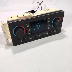 May include: A black car climate control panel with a digital display showing the temperature as 79 degrees Fahrenheit. The panel has knobs with blue and red indicators, and buttons for various functions. The top is off-white.