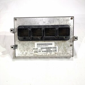May include: A silver-colored electronic control module with four black connector ports. The module has a rectangular shape with mounting holes on the sides. A label with text and barcodes is affixed to the front.