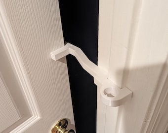 May include: White plastic door stop with a curved handle, installed on a white door frame.