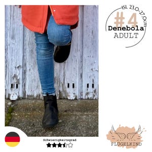 Könnte beinhalten: Eine Person trägt blaue Jeans und schwarze Stiefel. Die Person lehnt an einer verwitterten, weißen Holzwand. Ein orangefarbener Mantel ist oben im Bild zu sehen. Der Text lautet "#4 Denebola ADULT" und "ISL 23,0-27,0cm."
