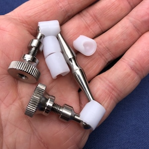 May include: A set of three silver metal knobs with white plastic caps. The knobs have a threaded shaft and a knurled head. The caps are cylindrical and have a smooth surface.