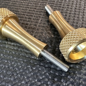 May include: Two gold-colored metal knobs with a threaded shaft. The knobs have a diamond-shaped pattern on the top and bottom.
