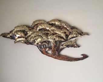 May include: A metal tree wall art piece with a gold and brown finish. The tree has a textured, layered design with a curved trunk and branches. The leaves are gold, and the trunk and branches are brown.