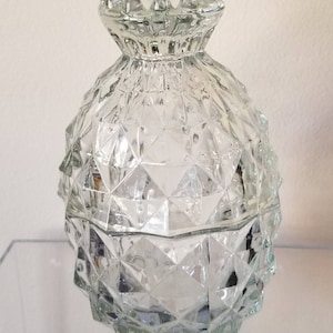 May include: A clear glass jar with a textured, diamond-shaped pattern. The jar has a lid with a scalloped edge.