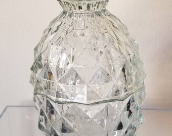 May include: A clear glass jar with a textured, diamond-shaped pattern. The jar has a lid with a scalloped edge.