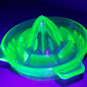 Peut inclure: Un presse-agrumes en verre vert avec un sommet cannelé et deux poignées. Le presse-agrumes est en verre d'uranium et brille sous une lumière noire.