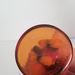 Puede incluir: La base de un jarr&oacute;n de vidrio transparente con un tono rojizo-naranja. El jarr&oacute;n tiene una base redonda y una abertura acampanada.