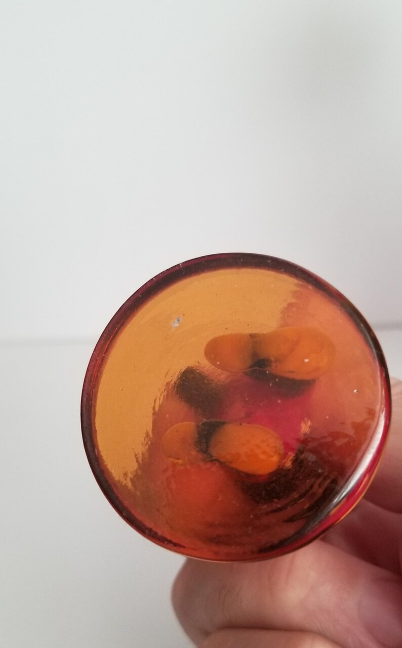 Puede incluir: La base de un jarr&oacute;n de vidrio transparente con un tono rojizo-naranja. El jarr&oacute;n tiene una base redonda y una abertura acampanada.