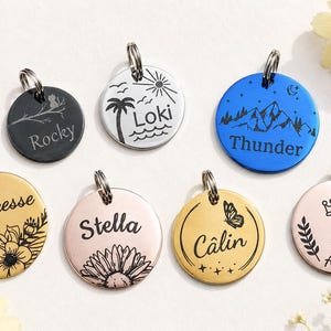 Op de afbeelding: Zeven ronde metalen naamplaatjes voor huisdieren met gegraveerde ontwerpen en namen. De plaatjes hebben diverse afwerkingen in zwart, zilver, blauw, goud en roségoud, met gravures zoals Rocky, Loki, Thunder, Princesse, Stella, Câlin en Ange.