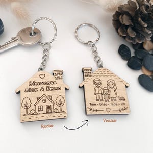 Peut inclure: Deux porte-clés en bois en forme de maison avec anneaux et chaînes en métal. Une face présente une illustration de maison avec le texte "Bienvenue Alex & Emma". L'autre face montre une illustration de famille avec les noms "Tom - Enzo - Jade - Lili" et une tortue.