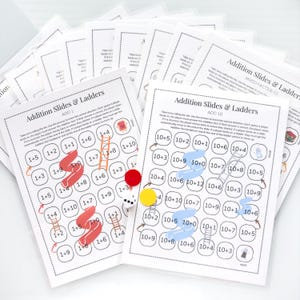 May include: Two printable game boards for an addition game called "Addition Slides & Ladders". The game boards are black and white with blue and red arrows, and ladders and slides are drawn in blue and red. The game boards are labeled "Add 1" and "Add 10".