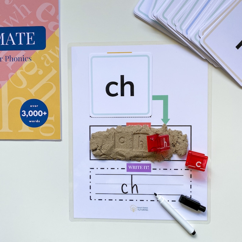 May include: A white dry-erase board with a green arrow pointing down to a brown sand tray. The sand tray has red letter tiles spelling out the word "ch". There is a white dry-erase marker and a white card with the letters "ch" in black on a light blue background.