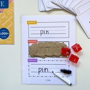 May include: A white card with the word "pin" written on it. There are three red letter blocks that spell out "pin" and a white dry-erase marker.