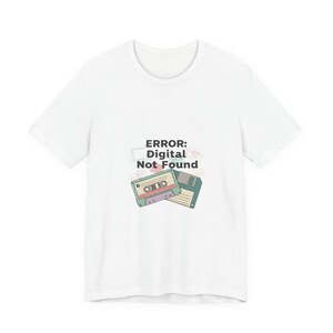 May include: White t-shirt featuring a retro design with a cassette tape and a floppy disk. The text "ERROR: Digital Not Found" is printed above the graphics. The shirt is made of a soft material.