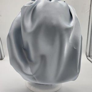 Pu&ograve; includere: Un cappuccio in raso azzurro, progettato per proteggere i capelli. Il cappuccio &egrave; raccolto nella parte superiore e ha una consistenza liscia e lucida. &Egrave; esposto su una forma arrotondata bianca su sfondo bianco.