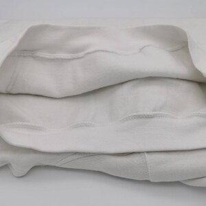 May include: White sweatshirt with a folded-over neckline, showing the inside of the fabric. The sweatshirt is made of a soft, comfortable material.
