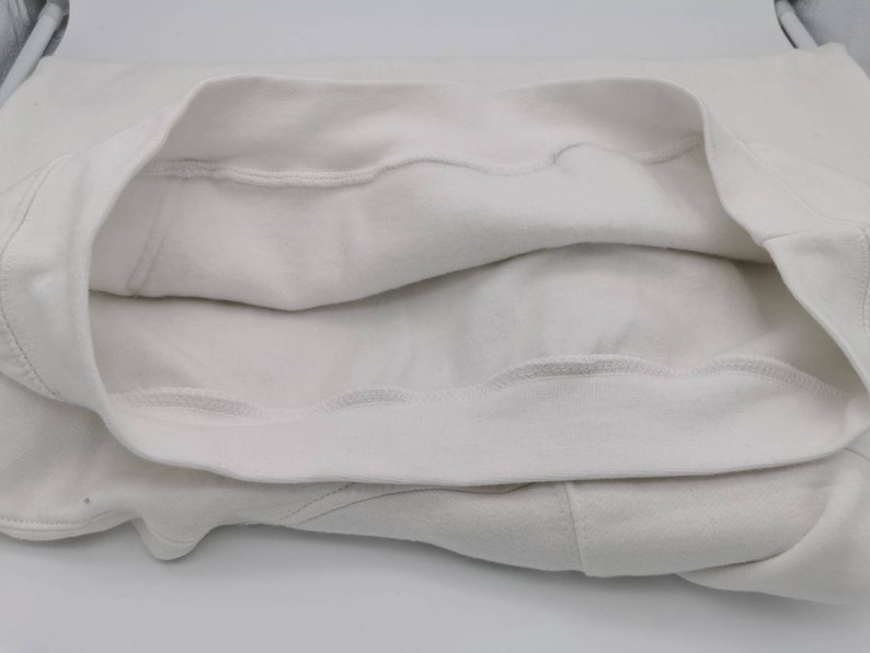 May include: White sweatshirt with a folded-over neckline, showing the inside of the fabric. The sweatshirt is made of a soft, comfortable material.
