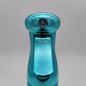 May include: A turquoise blue plastic spray bottle with a metallic finish. The bottle has a trigger sprayer and a clear nozzle.