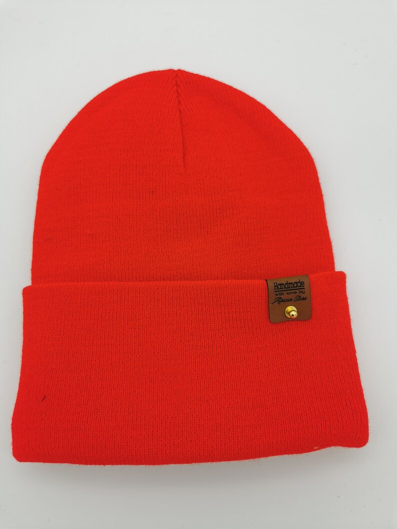 May include: A bright red beanie with a brown leather patch that says "Handmade with love by Fashion Finds".