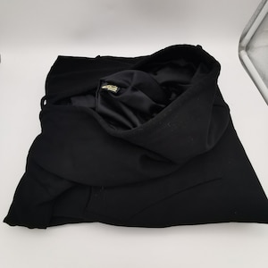May include: Black hooded sweatshirt folded on a white surface. The sweatshirt has a gold label on the inside of the hood.