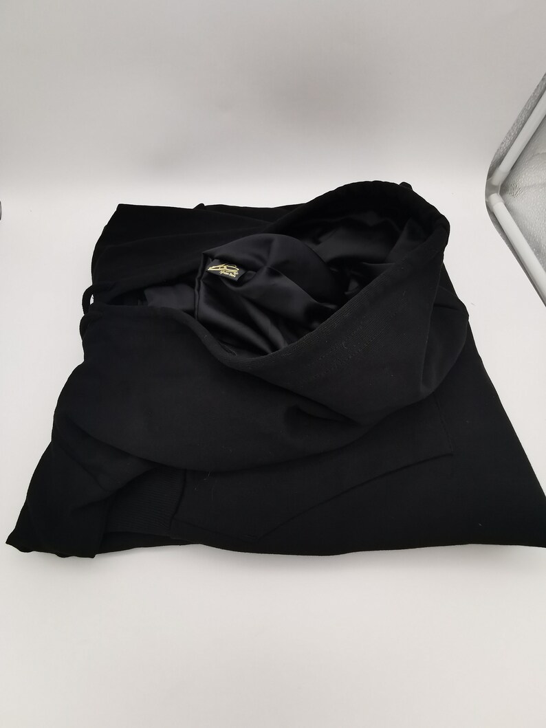 May include: Black hooded sweatshirt folded on a white surface. The sweatshirt has a gold label on the inside of the hood.