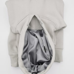 May include: A gray hooded sweatshirt with a drawstring and a gray satin lining. The hood is pulled up and the drawstring is visible.