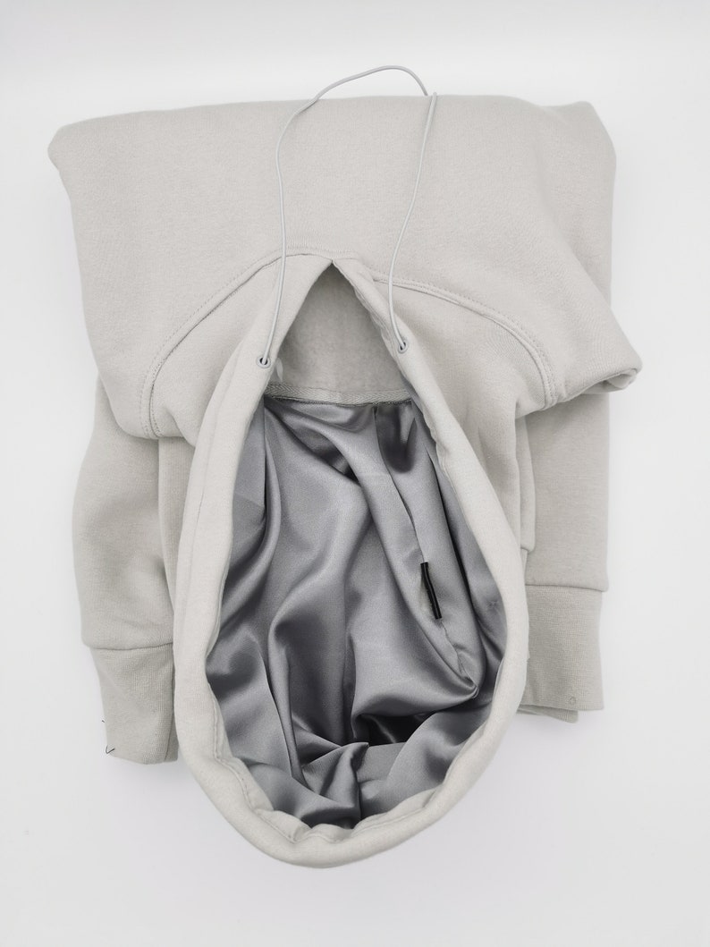 May include: A gray hooded sweatshirt with a drawstring and a gray satin lining. The hood is pulled up and the drawstring is visible.
