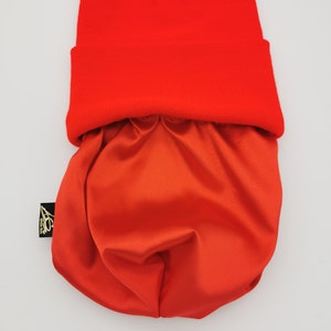 May include: A bright red beanie with a matching red satin lining. The beanie is folded down to show the lining.