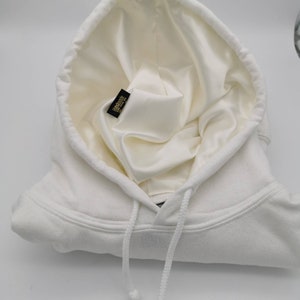 May include: White hooded sweatshirt with a white drawstring and a black label inside the hood that says "Handcrafted in Los Angeles".