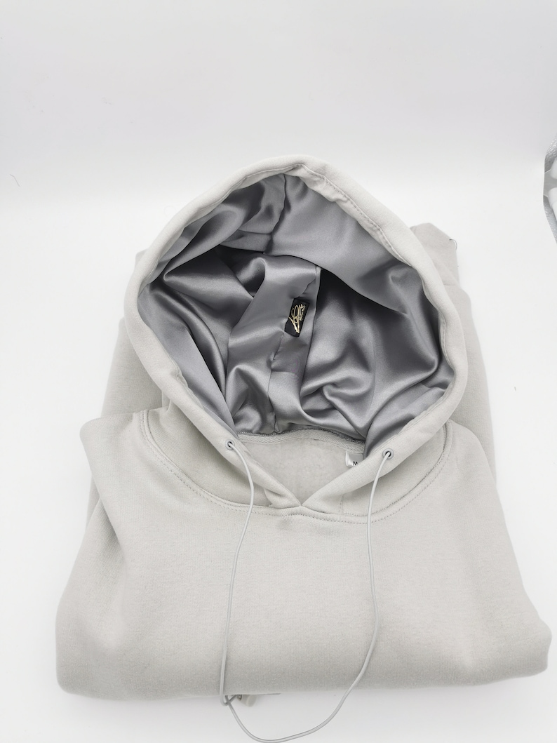 May include: A light gray hooded sweatshirt with a silver satin lining. The hood is folded down and the drawstring is visible.