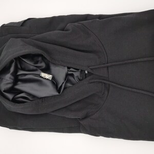 May include: Black hooded sweatshirt with a satin lining. The hood is folded down and the drawstring is visible.