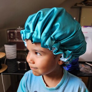 Pu&ograve; includere: Un cappuccio in raso turchese con fodera bianca. Il cappuccio &egrave; raccolto sul bordo e sembra essere realizzato in un tessuto lucido e liscio. Il cappuccio &egrave; progettato per proteggere i capelli.