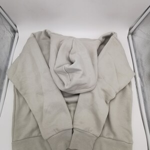 May include: A light gray hooded sweatshirt with a drawstring hood. The sweatshirt is folded and laid flat on a white surface.