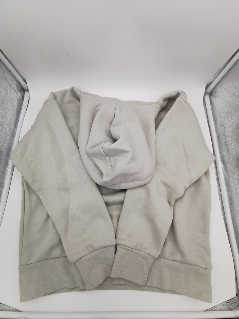 May include: A light gray hooded sweatshirt with a drawstring hood. The sweatshirt is folded and laid flat on a white surface.