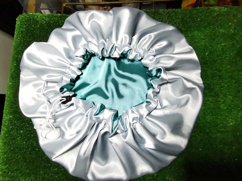 Pu&ograve; includere: Un cappuccio in raso argentato con interno turchese. Il cappuccio ha un bordo elastico arricciato e una chiusura con coulisse. Il prodotto &egrave; progettato per proteggere i capelli durante il sonno ed &egrave; realizzato in un tessuto liscio e lucido.